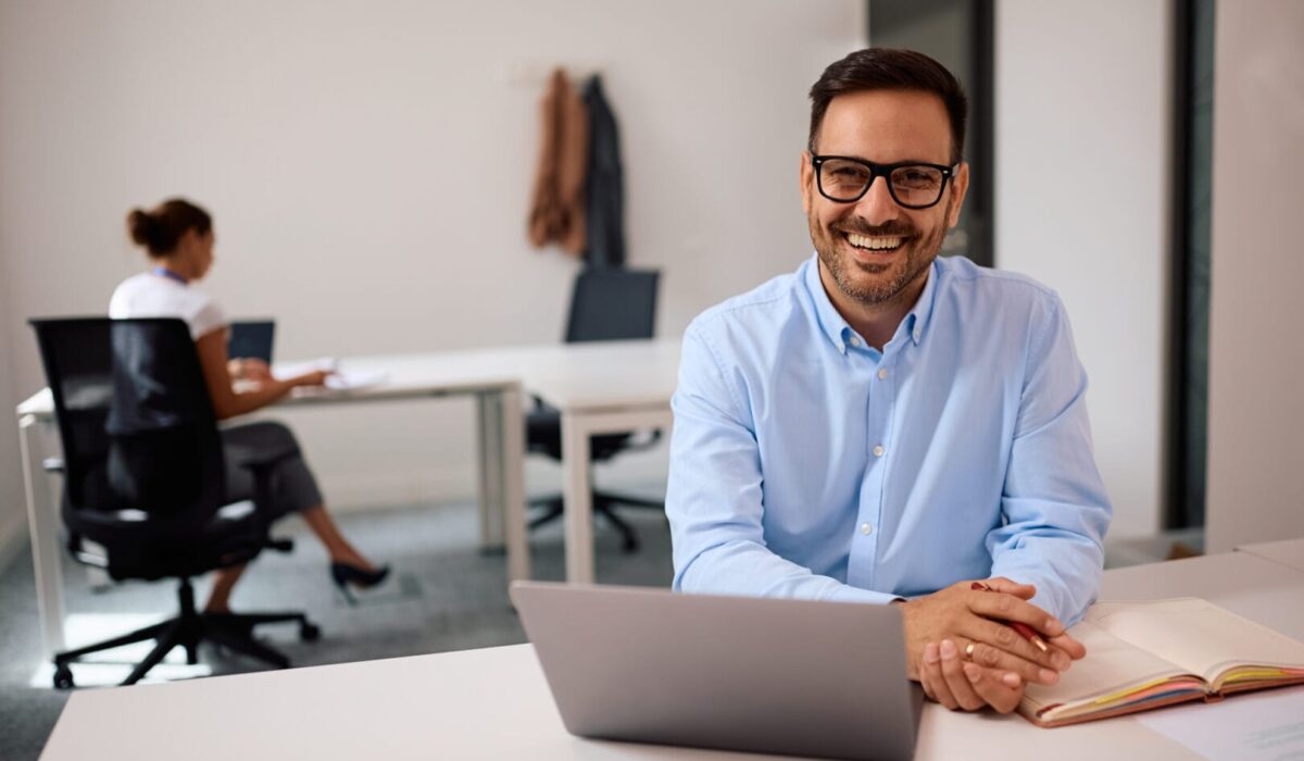 Happy entrepreneur working on laptop in shared workspace and looking at camera.